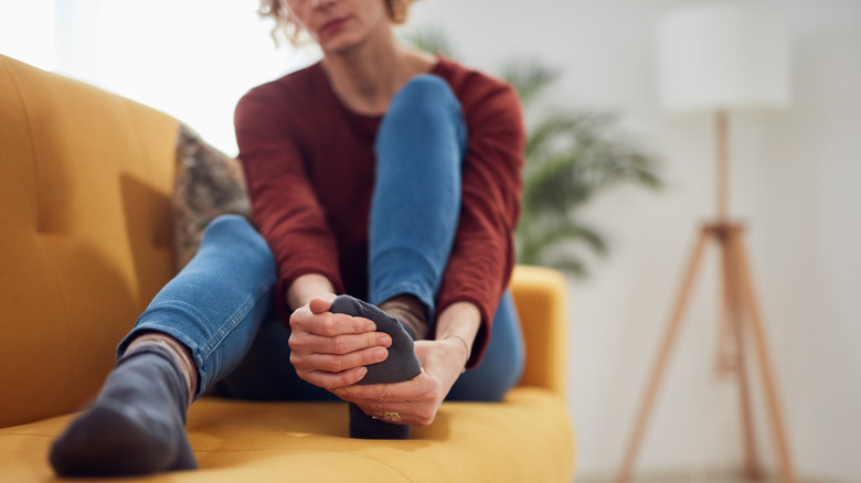 woman sitting on couch massaging foot