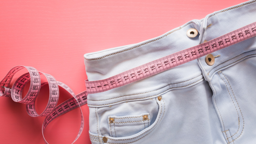 Close up of the waist of a pair of jeans wrapped in a tape measure