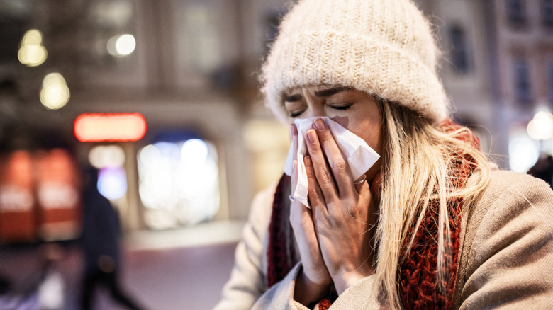 A woman dressed in winter clothes blowing her nose