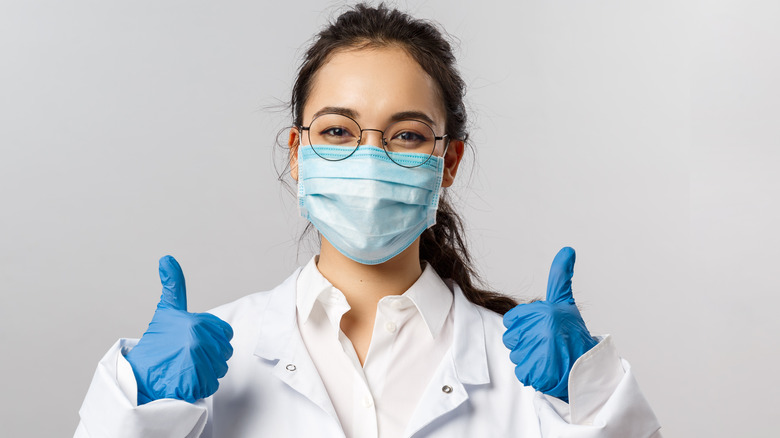 young doctor giving thumbs up with mask and gloves