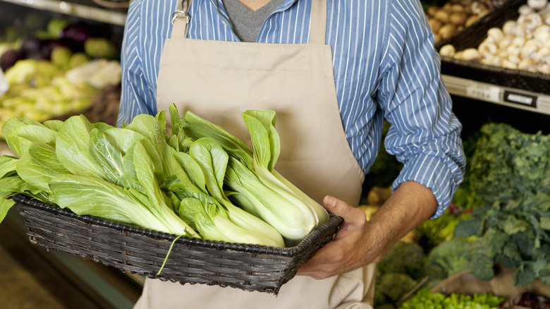 man holding basket filled with bok choy in market