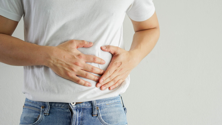 man in white t-shirt and jeans with hands on his abdomen 