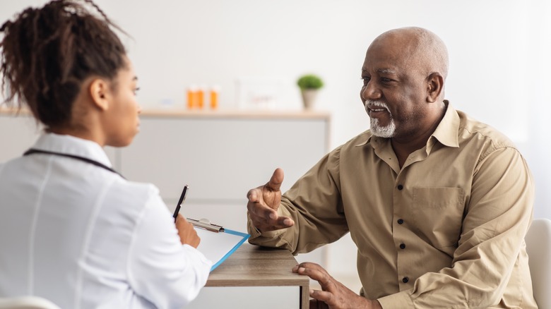 young Black female doctor speaking to elderly man while taking notes