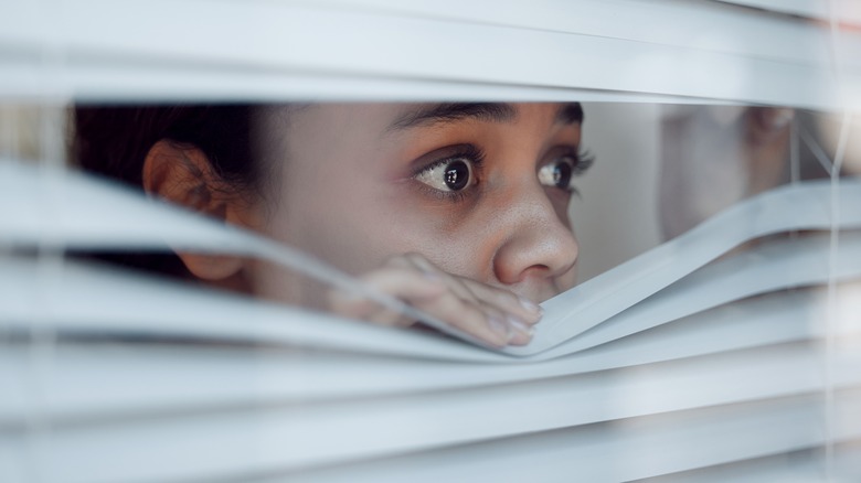 woman fearfully looking through window blinds