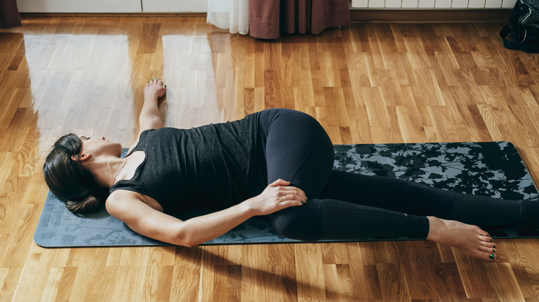 A woman practicing a reclined spinal twist on a wood floor