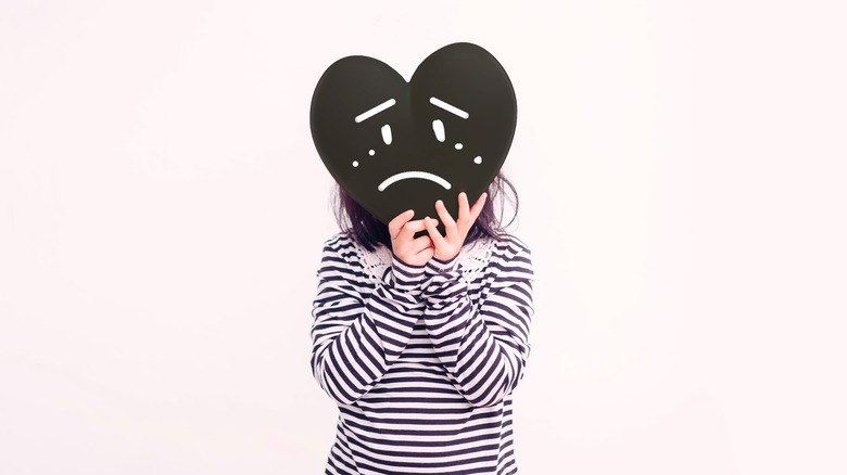 Kid holding a black heart with a sad face