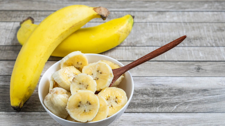 A bowl of sliced bananas next to whole bananas