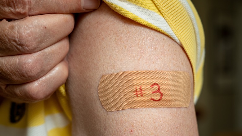 Close up of person rolling up sleeve to reveal a bandaid on upper arm reading "#3"