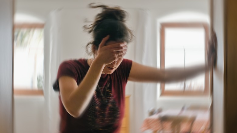 Woman standing against wall holding her head feeling dizzy