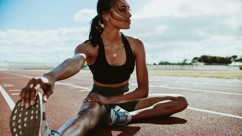 Woman runner stretching leg muscles, touching her shoes, and looking away.