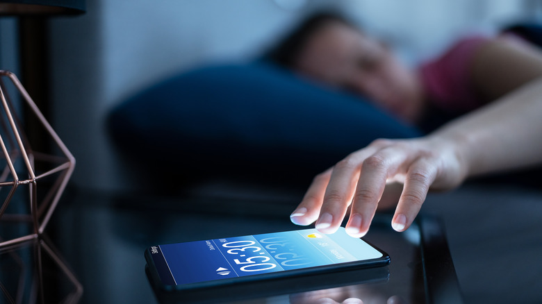 Woman in bed reaching for phone with alarm