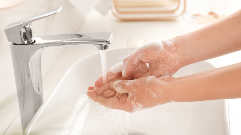Soapy hands under running water in sink
