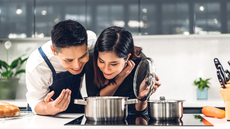 Young couple bent over stovetop pot 