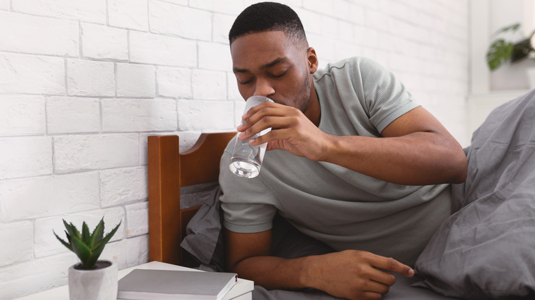 young man drinking water in bed