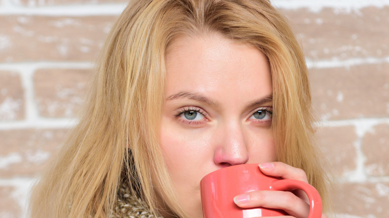 Woman drinking from mug and holding a tissue.