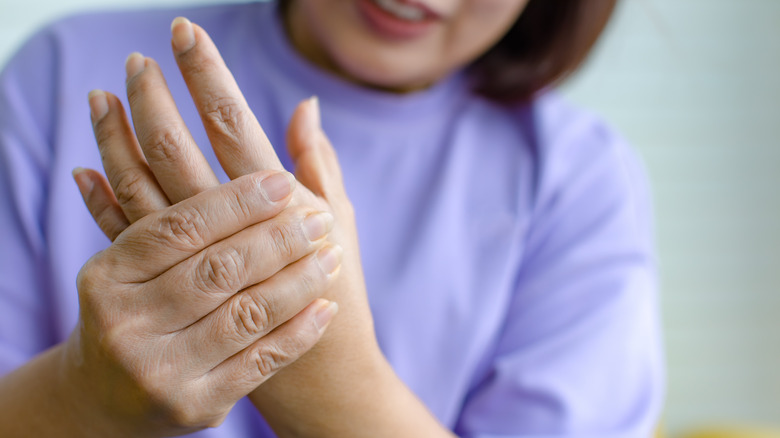 Woman in purple shirt holding her left hand in pain