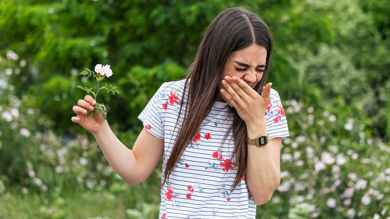 Woman sneezing while holding flower outside