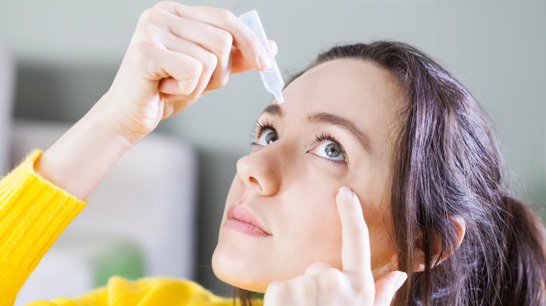 Young woman putting drops in eyes