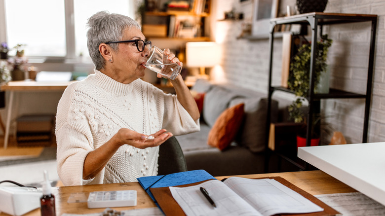 An older woman taking medication with a glass of water