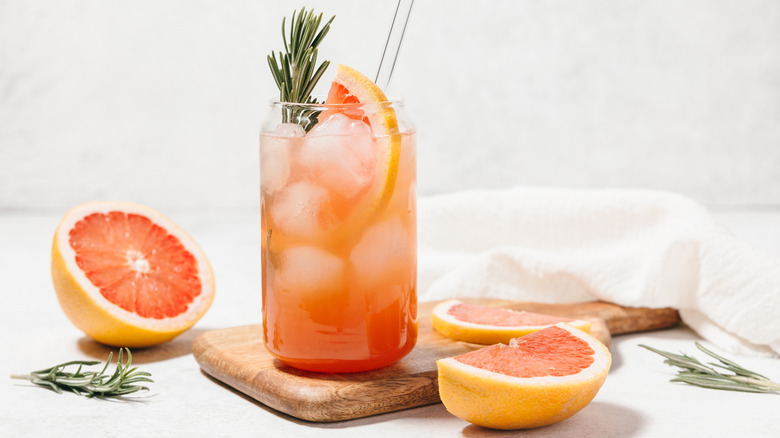 A tall glass of grapefruit juice surrounded by sliced grapefruit