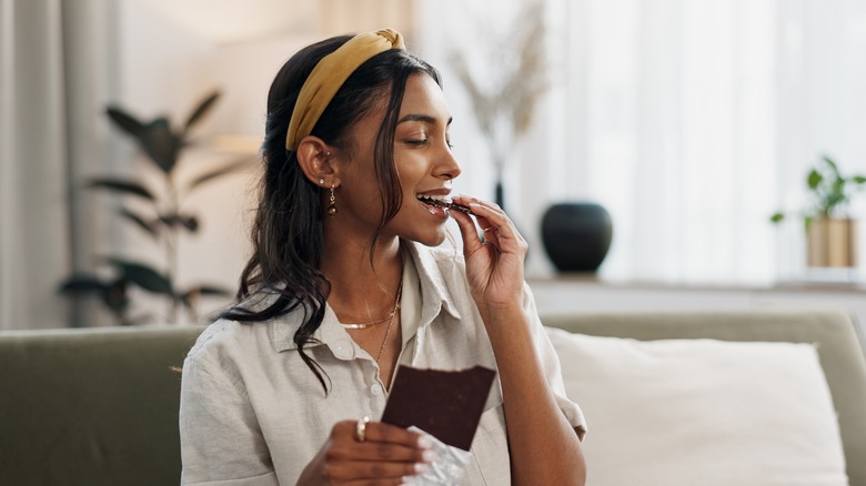 A woman eating a dark chocolate candy bar while sitting on her couch