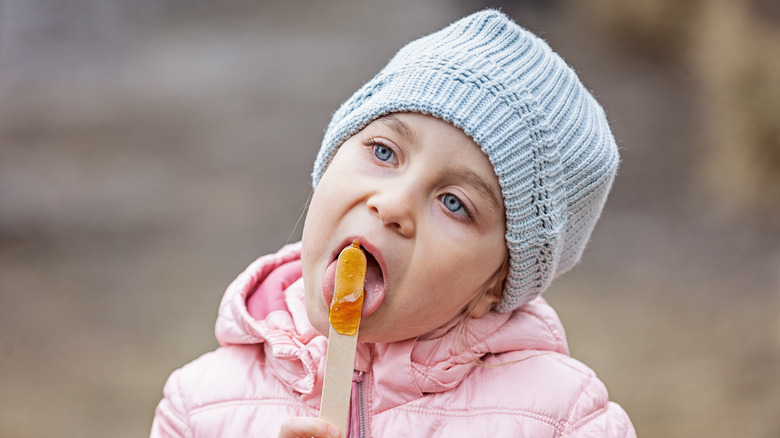 A little girl eats maple syrup taffy on a stick