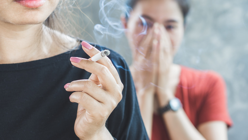 Woman smokes a cigarette while another covers her nose