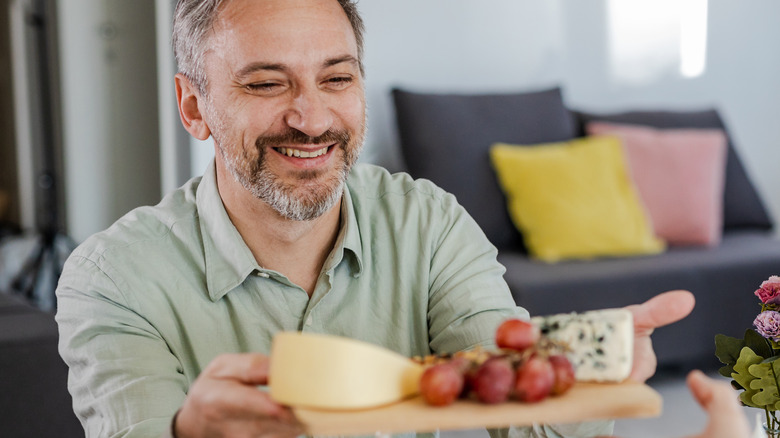 smiling white-haired man holding cheese board