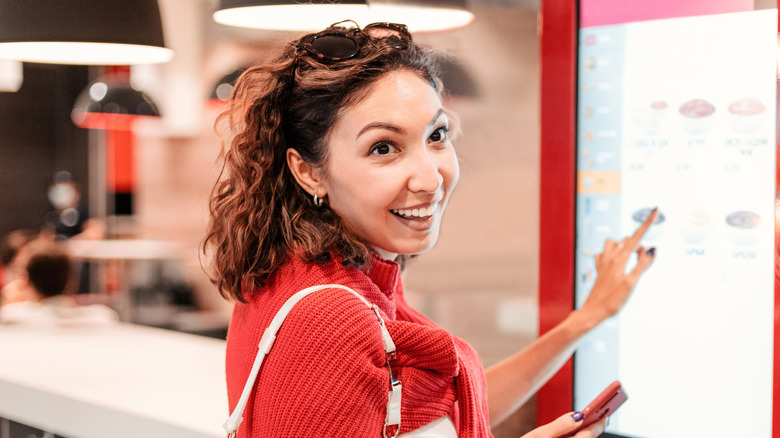 A woman ordering fast food from a touchscreen menu board