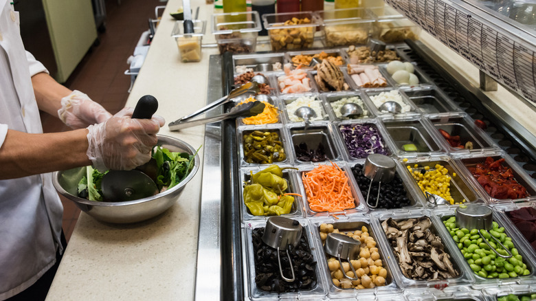 man preparing a salad in front of a variety of ingredients