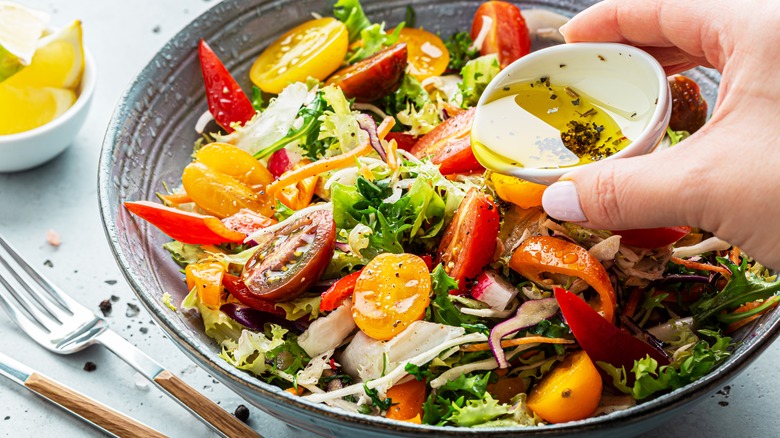 woman's hand adding oil-based dressing to salad