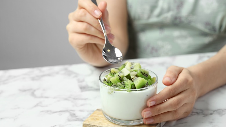 Hands holding cup of yogurt with kiwi