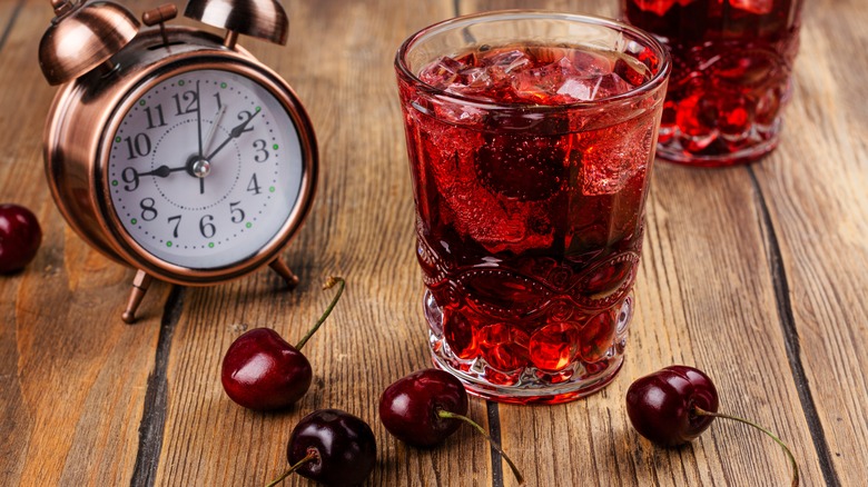 Glass of cherry juice next to clock