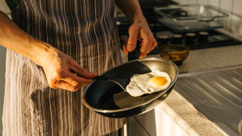 A man's hands holding a skillet with a fried egg