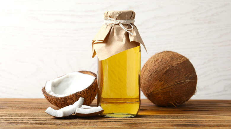 A bottle of coconut oil between a coconut