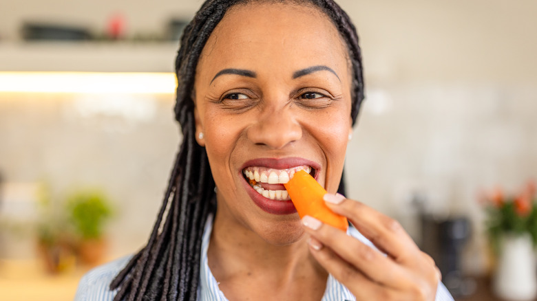 smiling woman eating a carrot in a kitchen