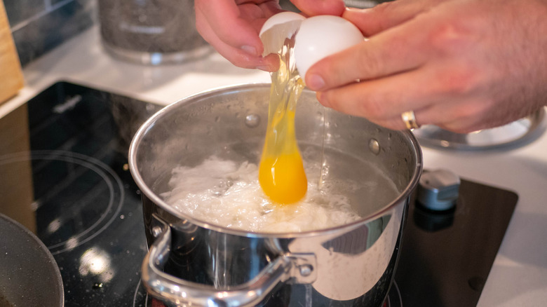 hands cracking egg in boiling water