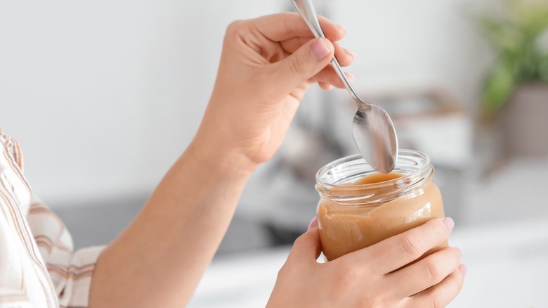 woman's hand putting spoon in peanut butter jar