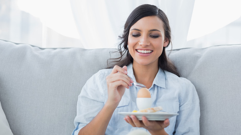 smiling woman eating egg on plate