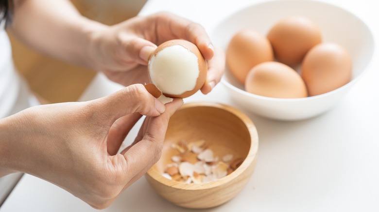 woman peeling hard-boiled egg into bowl