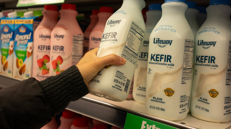 A woman's hand reaching for kefir milk from a grocery shelf