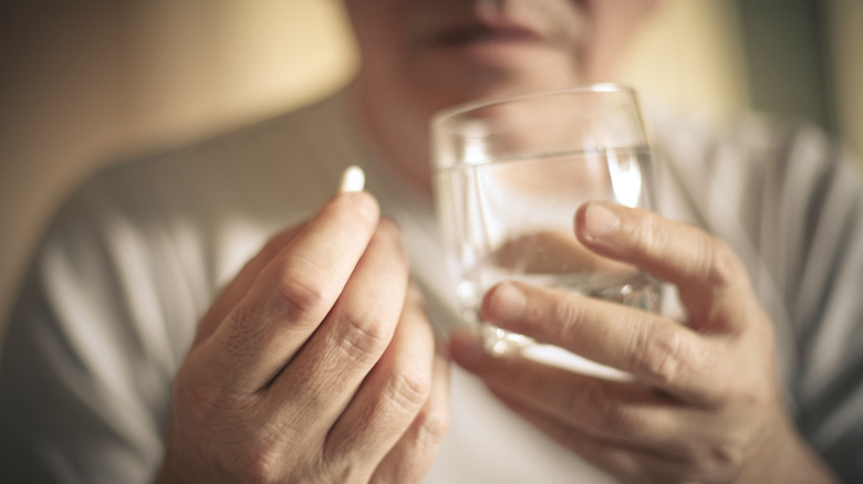 older man's hands holding water and medication