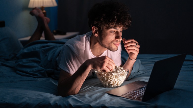 man lying in bed watching video on laptop