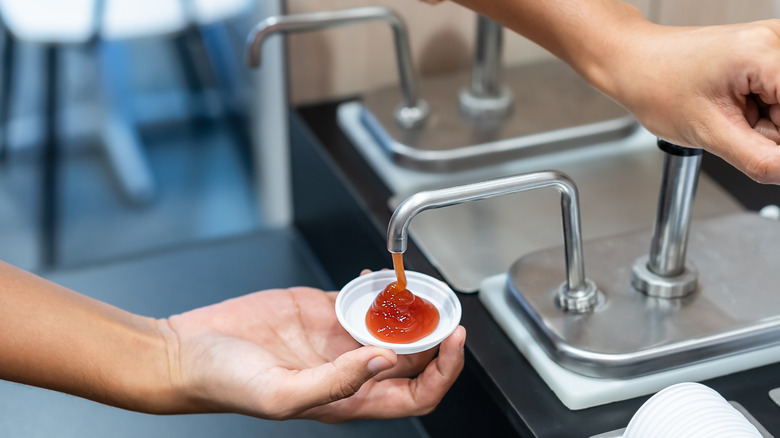 A hand of a man pumping ketchup into a paper cup