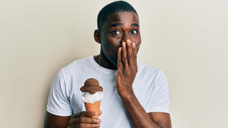 surprised man holding ice cream cone and covering mouth