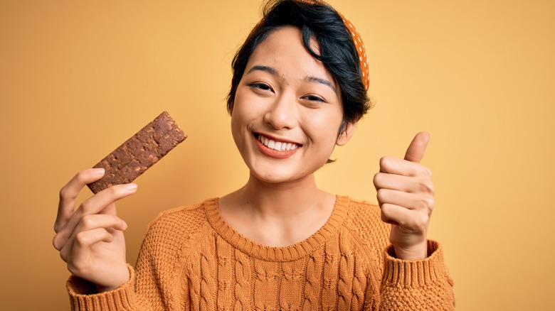 Woman holding a protein bar in her hand, smiling