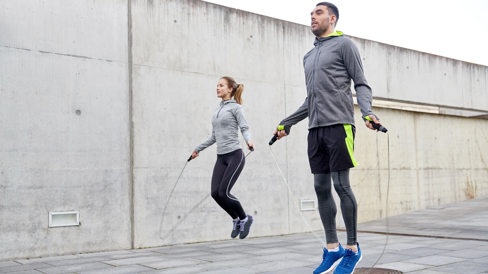 A man and a woman jump rope outdoors
