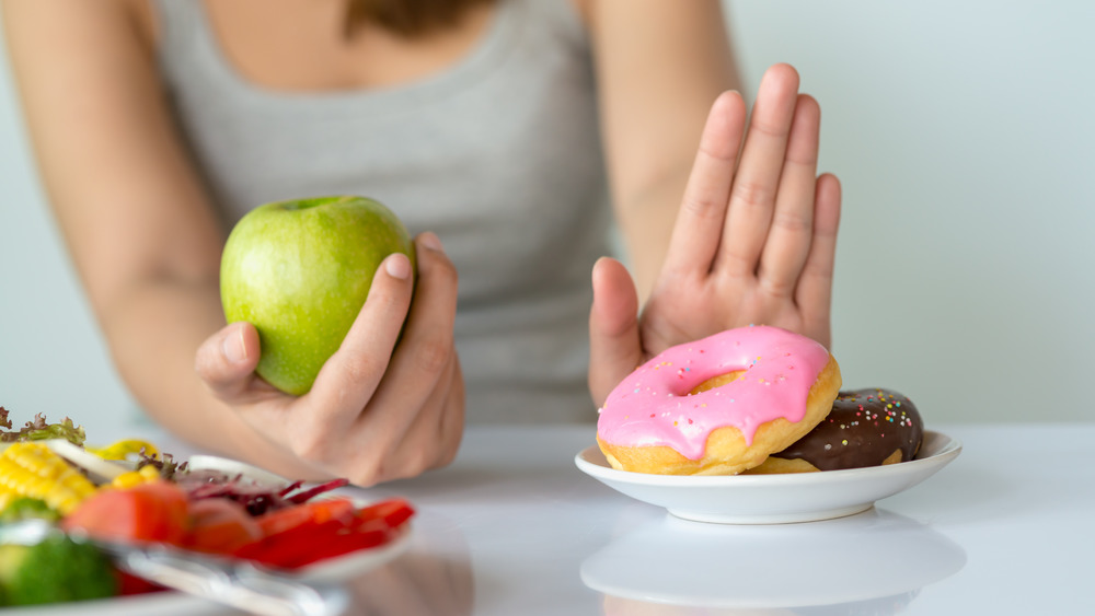 woman holding an apple, pushing away donuts