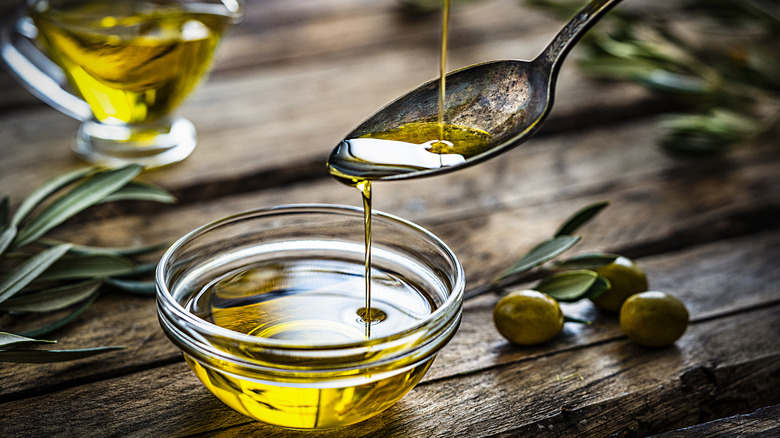 olive oil being dripped onto a spoon and into a small jar