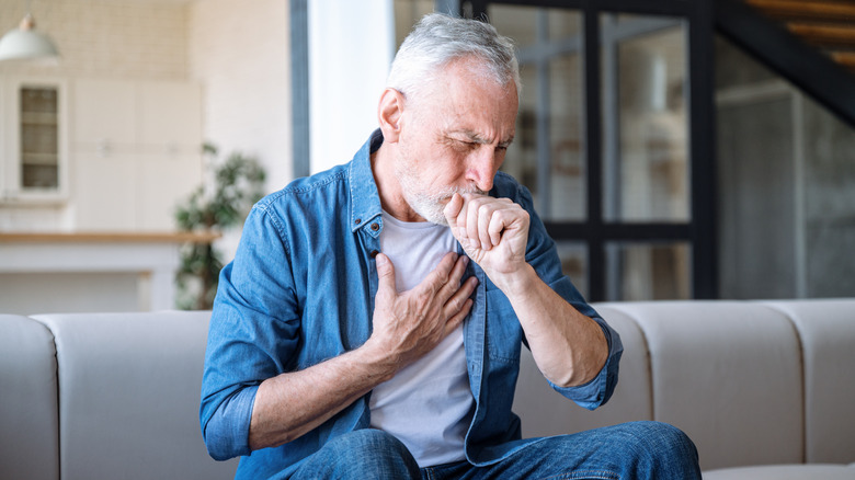 older man coughing while sitting on his couch